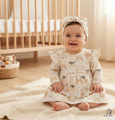 Baby in a patterned dress sitting on a blanket in a nursery