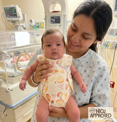 Mother holding premature baby in NICU hospital ward. Baby is wearing Duper DuDu adaptive organic romper in Bakery Dreams print. Soft fabric for kangaroo care.