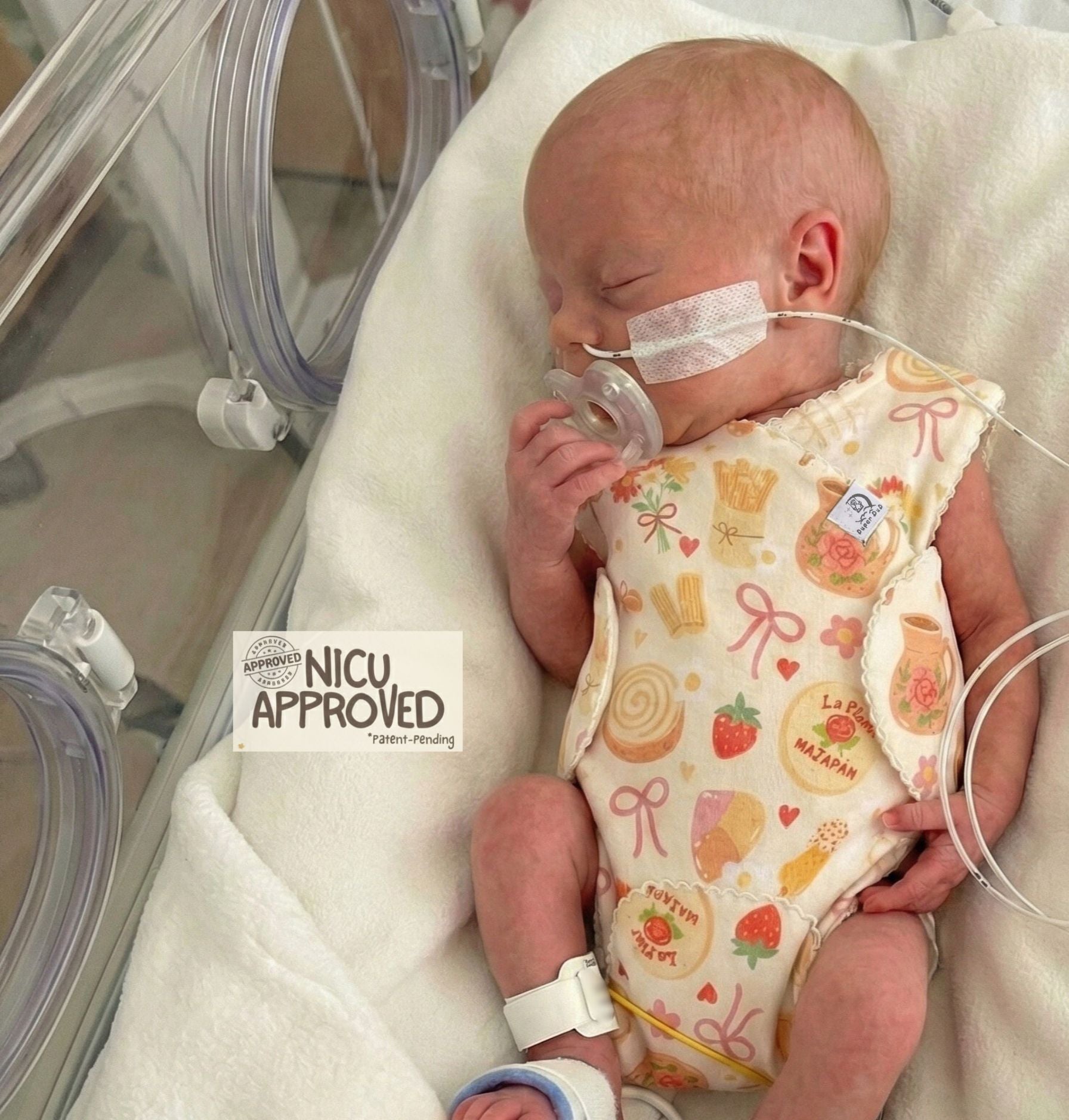 Premature baby sleeping in NICU incubator wearing Bakery Dreams organic romper. Design allows easy access for medical wires and feeding tubes. NICU Approved. Duper DuDu